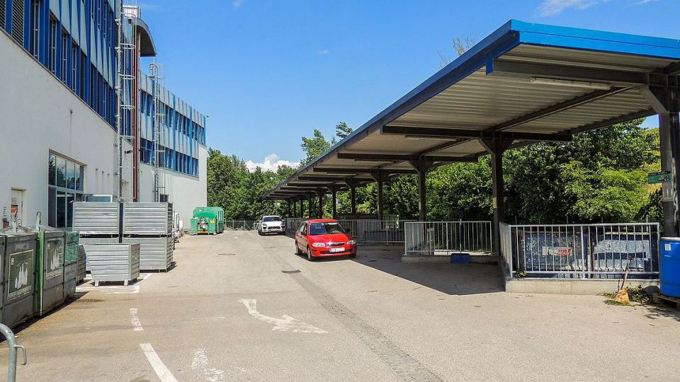 rotes Auto auf einem Altstoffsammelhof vor den Containern