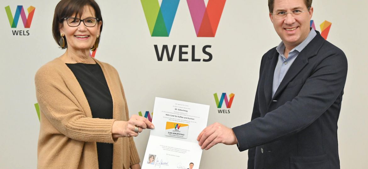 Bürgermeister Dr. Rabl und Stadträtin Josseck-Herdt, Referentin für Generationen, halten gemeinsam mit Abstand eine Geburtstagskarte mit der Wels-Card