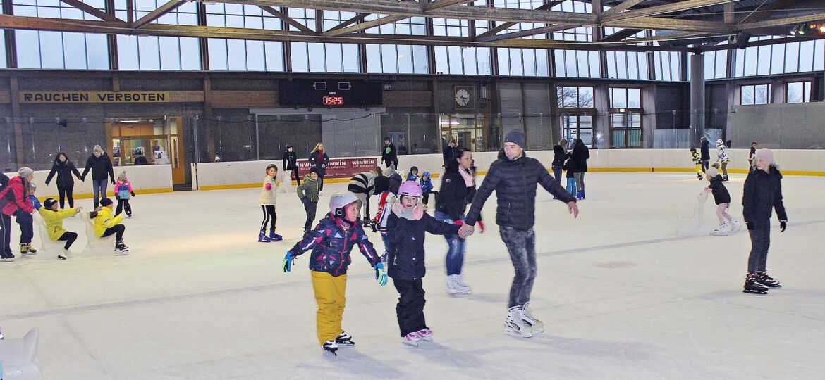 Erwachsene und Kinder die gemeinsam Runden auf dem Eis in der Welser Eishalle ziehen