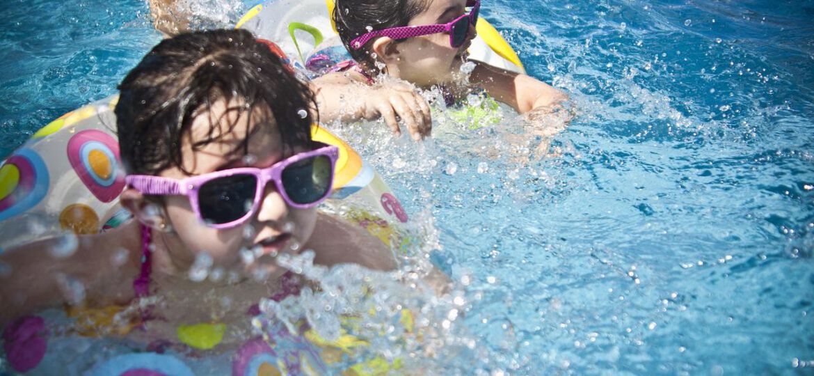 Zwei Kleinkinder mit Schwimmreifen und Schwimmbrille beim Plantschen.