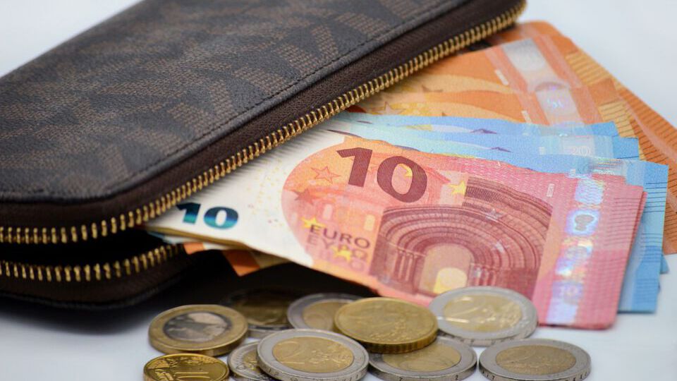 Eine halb offene Geldbörse, aus der verschiedene Euro Scheine heraus ragen, einige Euro Münzen davor