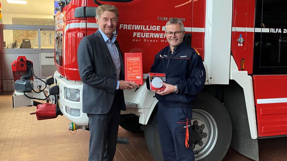 Vizebürgermeister Kroiß und Ing. Humer vor einem Feuerwehrauto mit Löschdecke und Rauchwarnmelder
