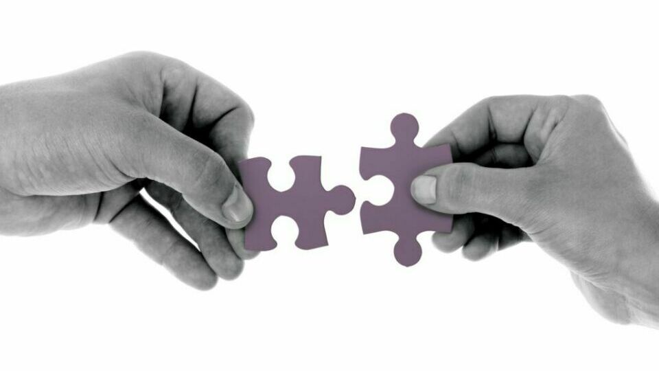 Zwei Hände halten jeweils ein zueinander passendes Puzzleteil.